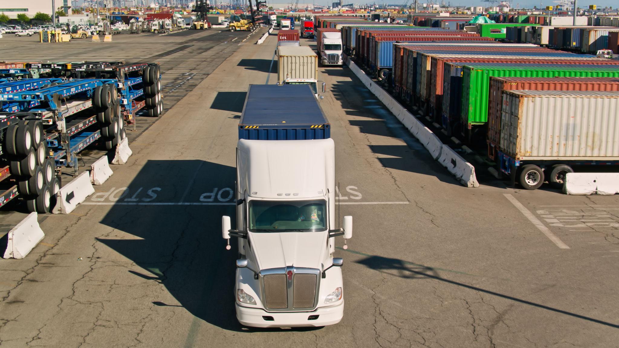 Container trucks at an intermodal yard with stacked containers, landed cost and logistics flow
